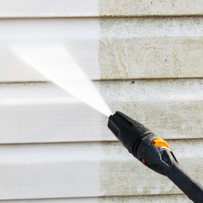Pressure washing white siding with a black nozzle spraying water