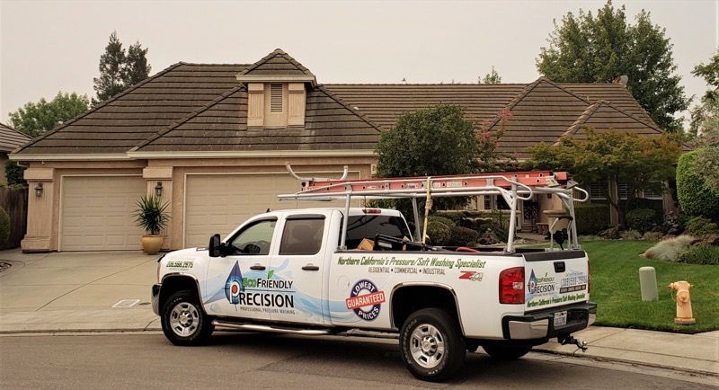 Utility truck parked in front of a suburban house, carrying a roof ladder rack and service equipment.