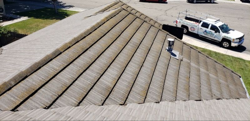 Roof with weathered shingles and a worker on a steep slope beside a white utility truck