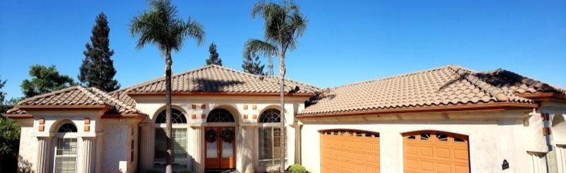 Single-story stucco house with red-tile roof, arched entry, garage, and palm trees in front