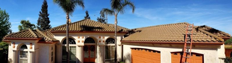 Mediterranean-style house with red tile roof, arched entry, palm trees, and a bright blue sky