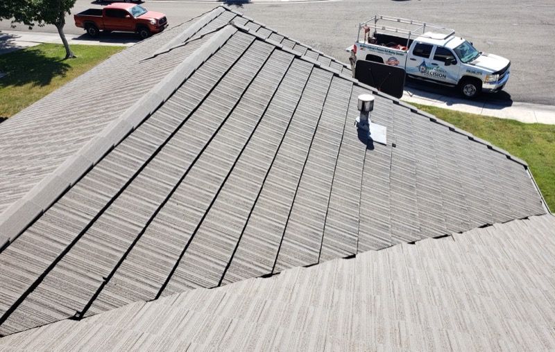 Worker on a shingled roof near parked trucks, viewed from above.
