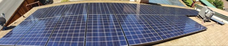 Solar panels mounted on a roof with a nearby air conditioner unit and blue sky.