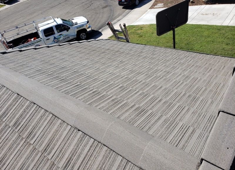Roof with a white work truck parked on a street below, near a driveway and lawn.