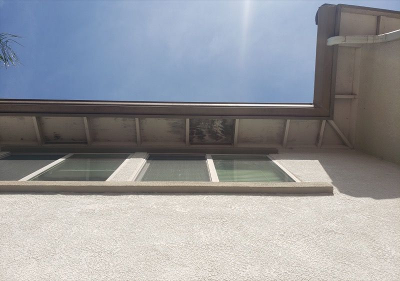 Upward view of a building wall, windows, and roofline against a bright blue sky
