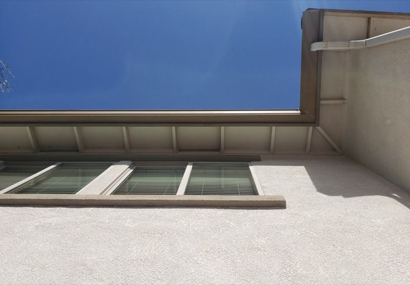 Low-angle view of a building exterior with windows, roofline, and bright blue sky.