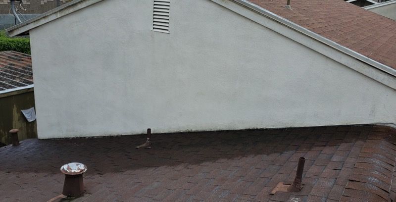 Brown shingle roof with a white house wall and two roof vents, viewed from above