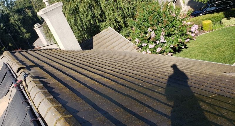 Roof shingles viewed from a rooftop, with a chimney and a shadow cast on the sloped roof.