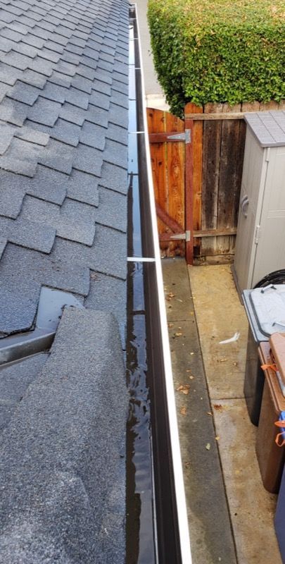 Narrow side alley between a house roof and fence, with a concrete path and storage bins.