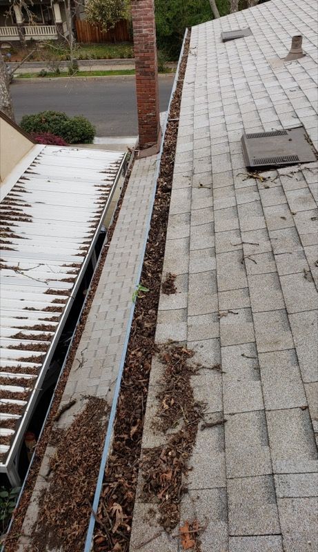 Rooftops with heavy snow buildup along a narrow gutter between two houses.