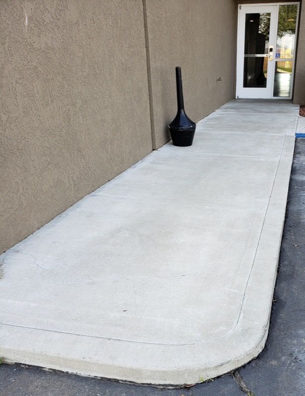 Concrete wheelchair ramp beside beige building leading to a doorway, with a black lantern nearby