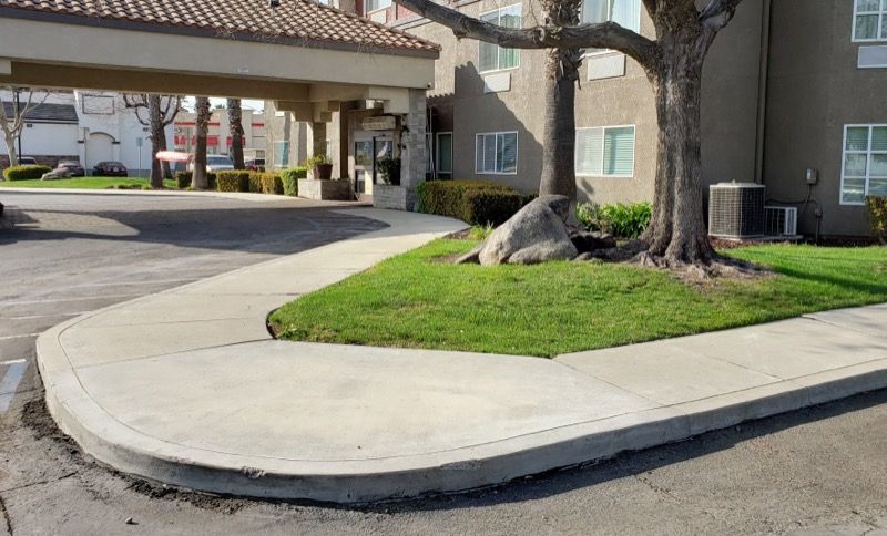 Apartment driveway curb with a landscaped grassy island and a large tree under a covered entrance