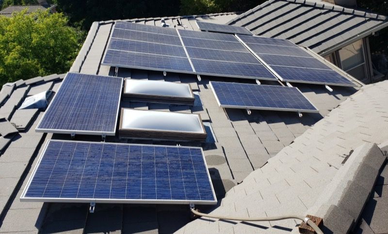 Solar panels installed across a gray shingled roof in bright daylight.