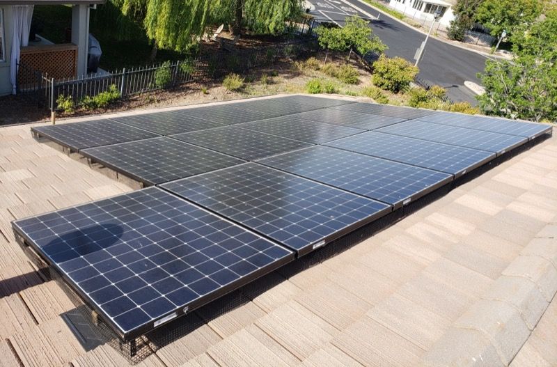 Solar panels installed on a rooftop under daylight, with nearby greenery and a paved street visible.