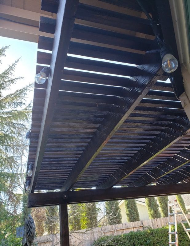 Open metal carport roof with slats, viewed from below against blue sky and trees