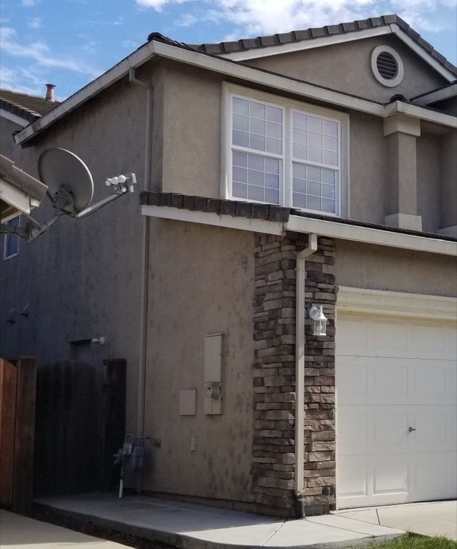 Two-story suburban house with beige stucco, white garage door, and a satellite dish on the side.