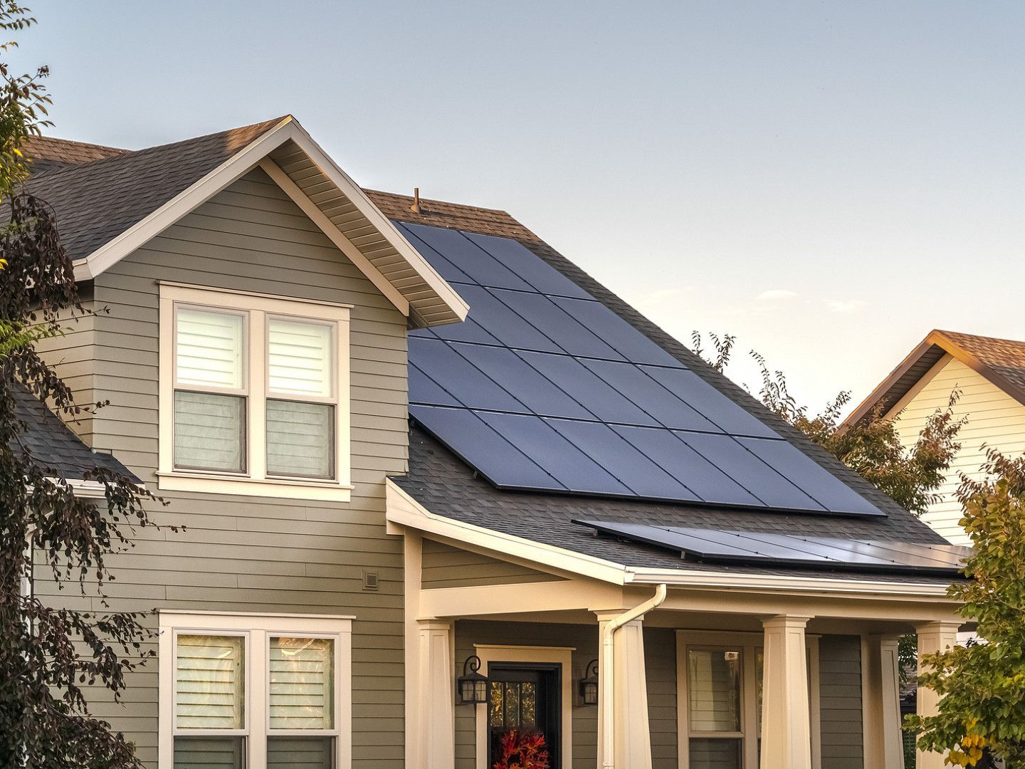 Suburban house with a gray shingled roof and black solar panels at sunset