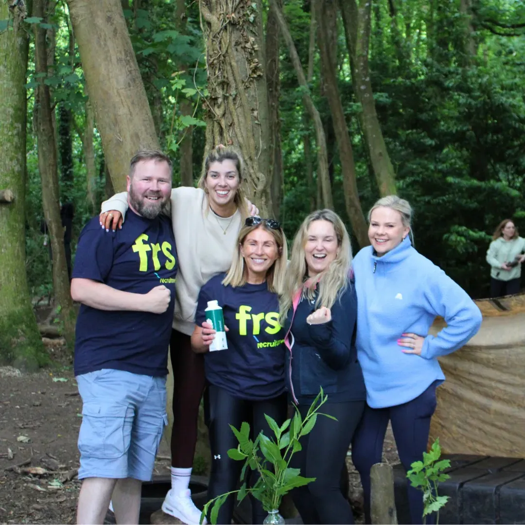 Group of five people smiling in a forest. They wear blue and tan shirts. One person holds a water bottle.