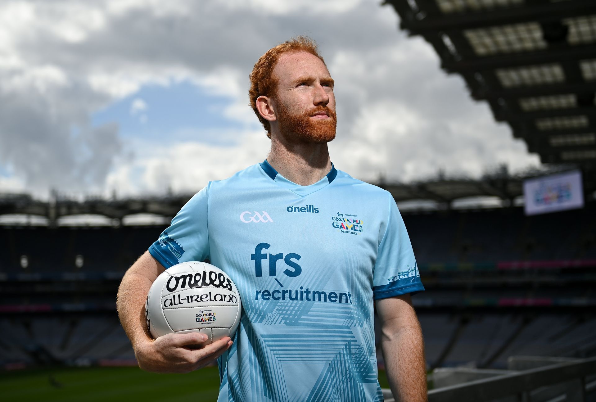 Man in light blue jersey holding a football at a stadium.