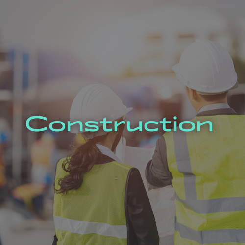 Two people in hard hats and safety vests on a construction site looking at plans.