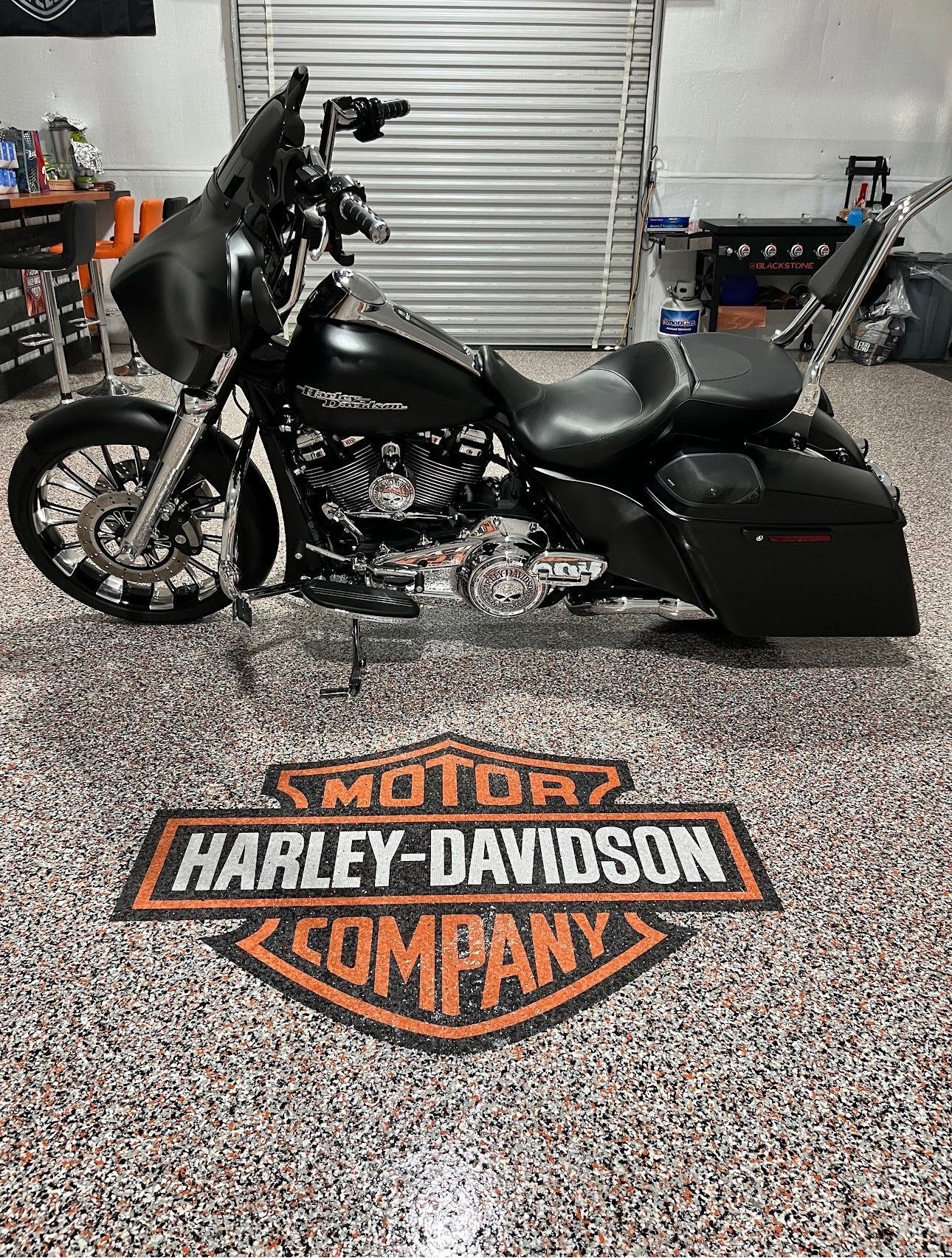 Black Harley-Davidson motorcycle in a garage, parked over a Harley-Davidson logo floor mat.