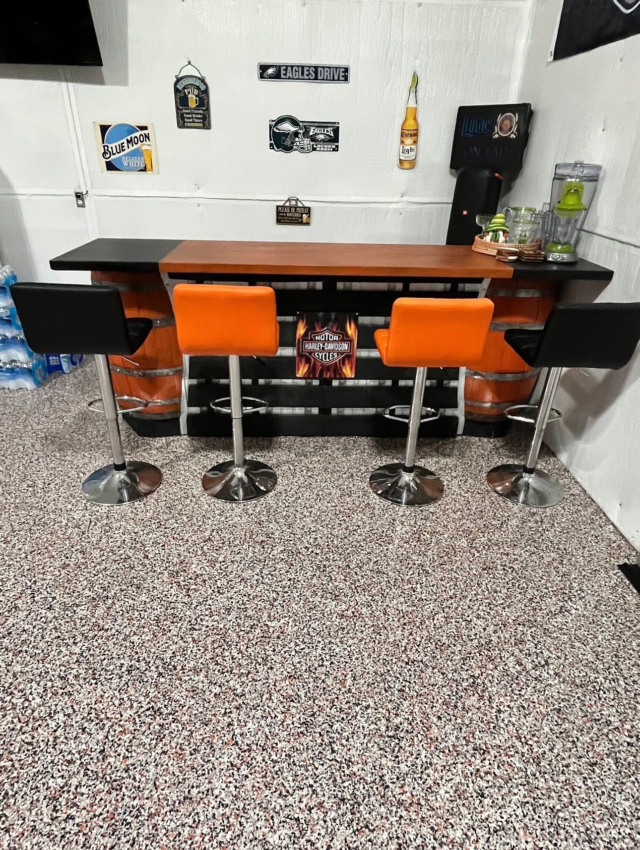 Retro-style bar counter with three orange stools in a small room with wall decor and a coffee machine