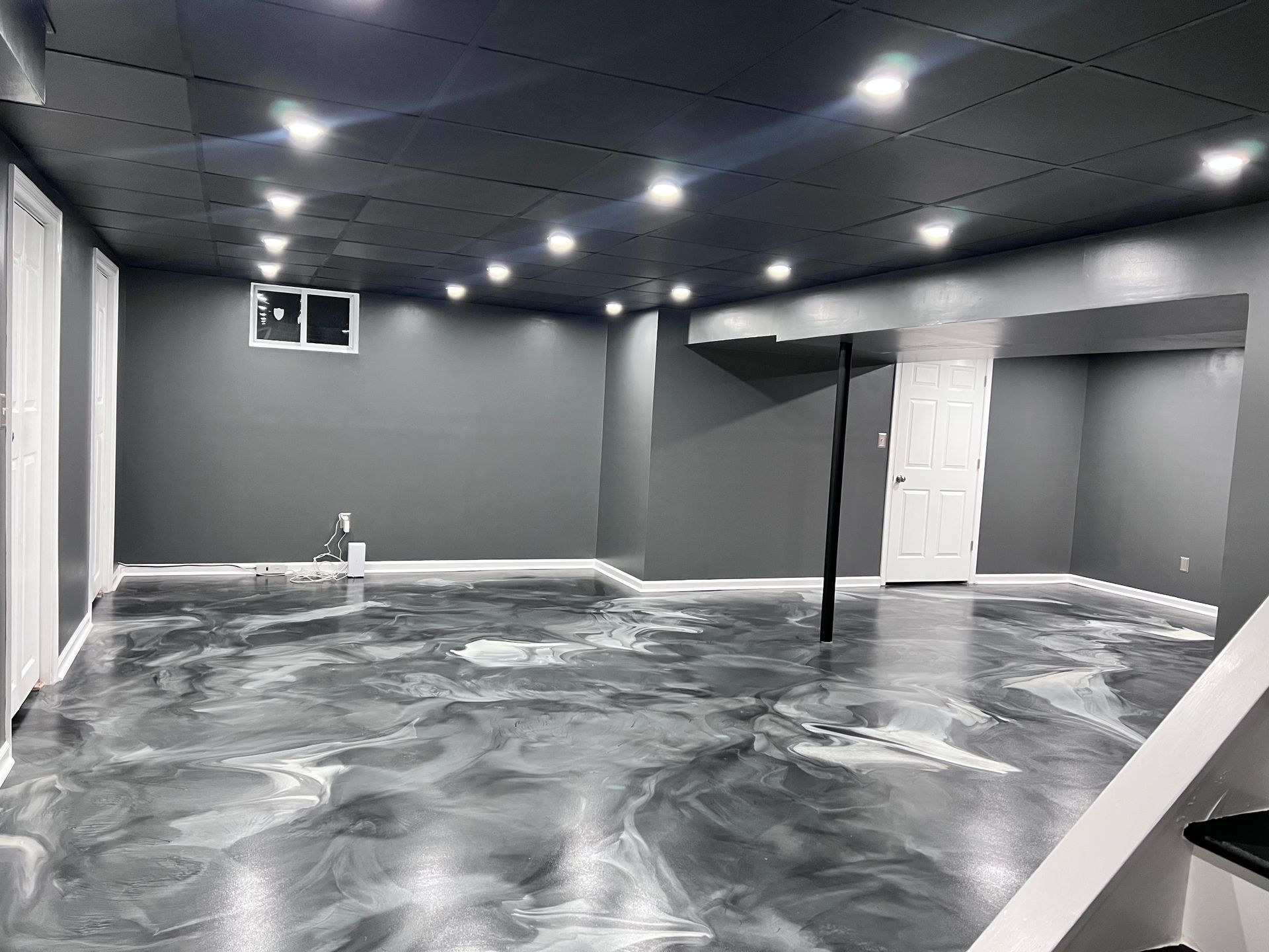 Empty gray room with black ceiling, marbled floor, and a central support pole.