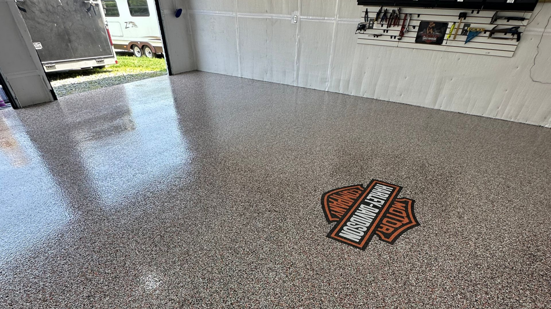 Empty speckled concrete floor in a garage with a Harley-Davidson logo mat near the center