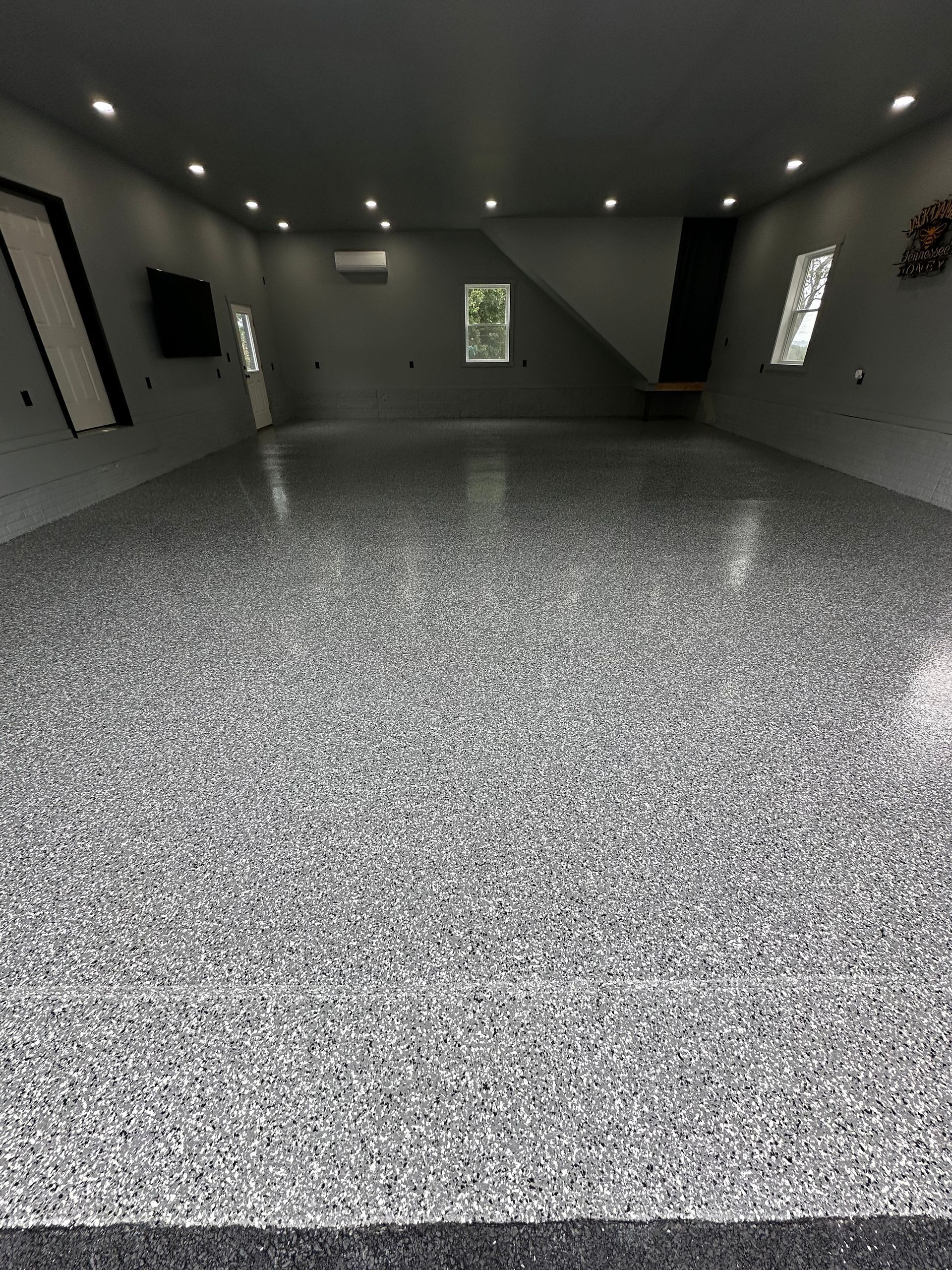 Empty modern room with gray speckled floor, dark ceiling, recessed lights, and small windows