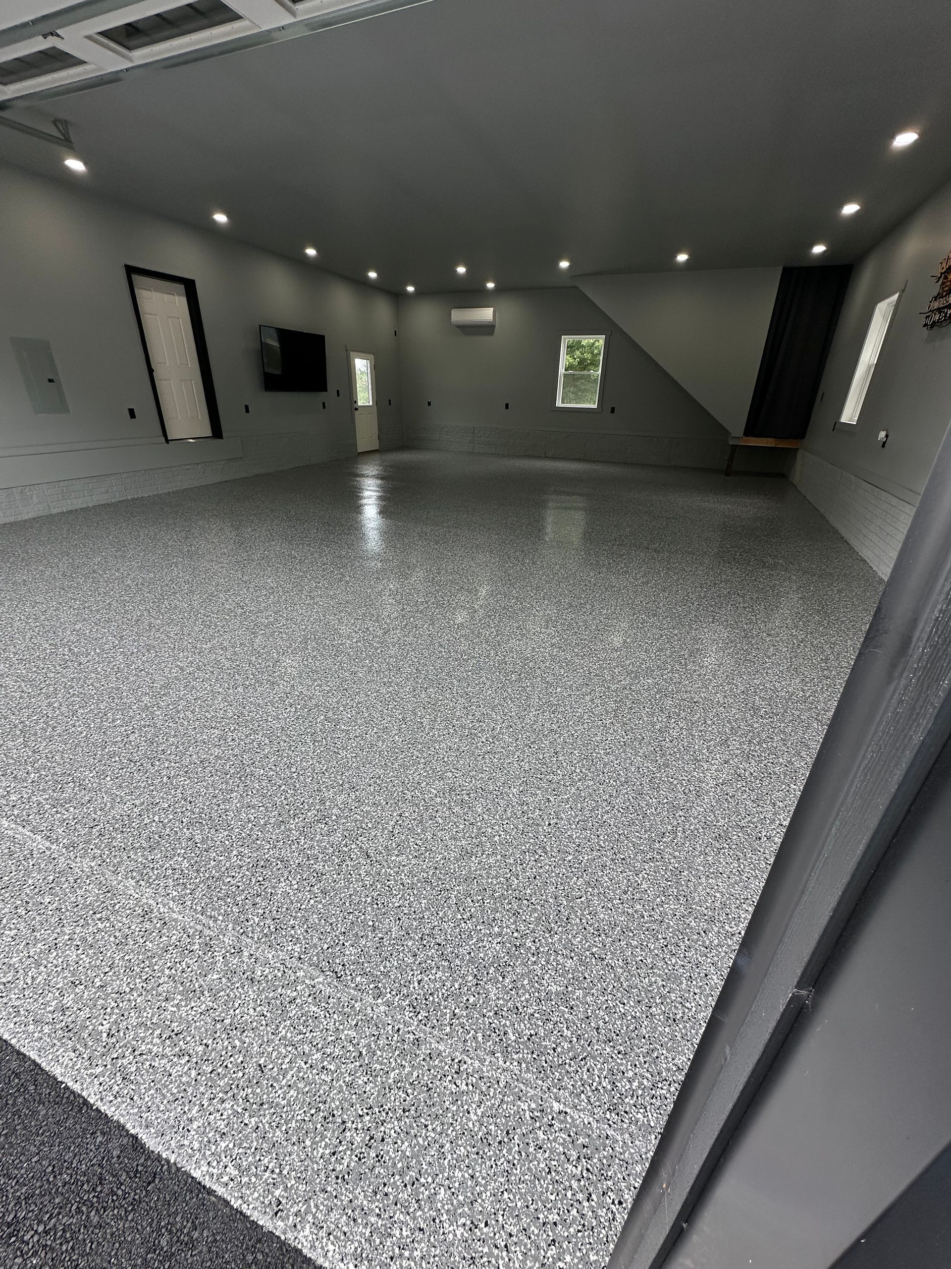 Empty modern room with gray-speckled floor, recessed lights, and a wall-mounted TV.