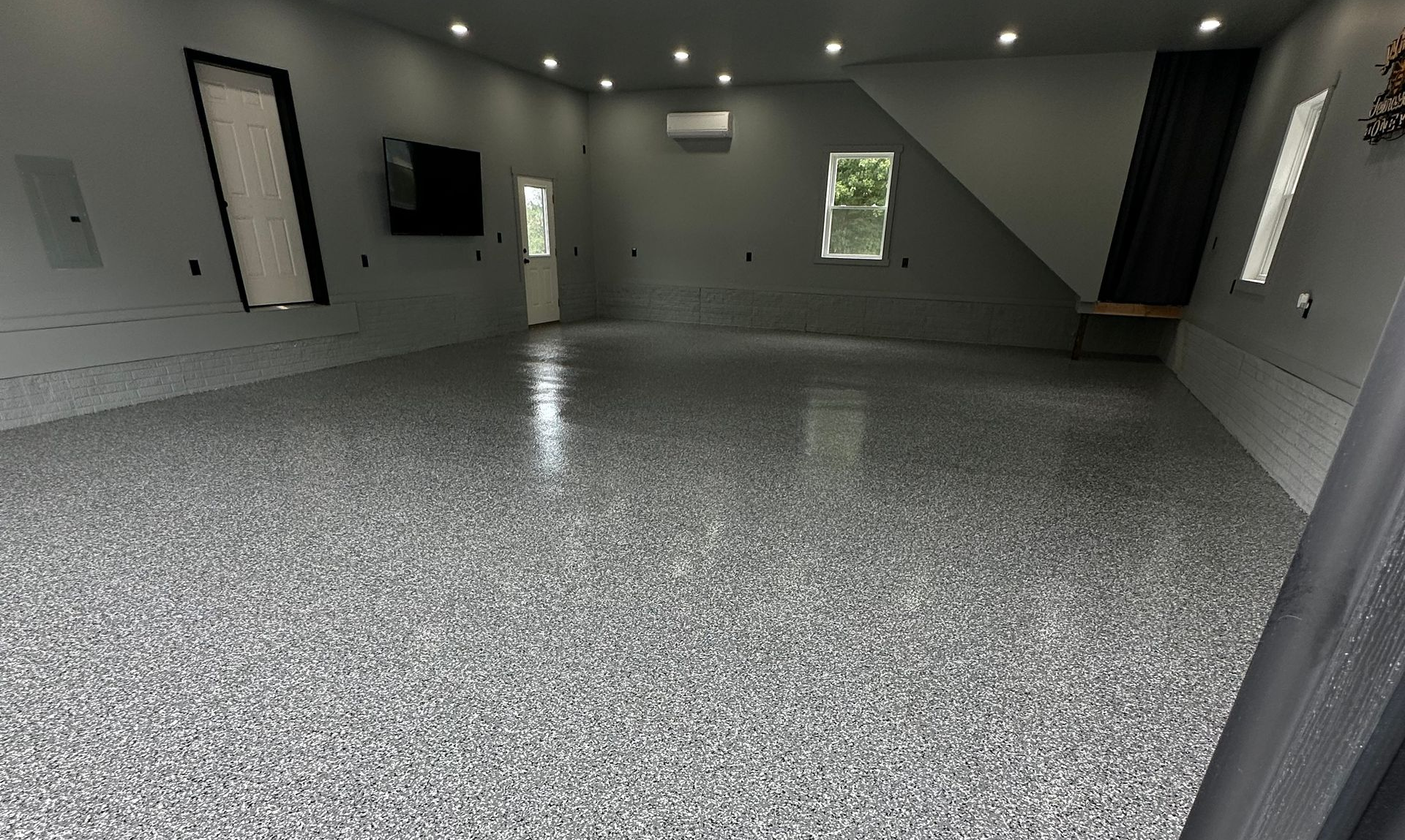 Spacious empty room with glossy speckled gray floor, recessed lights, and narrow windows.