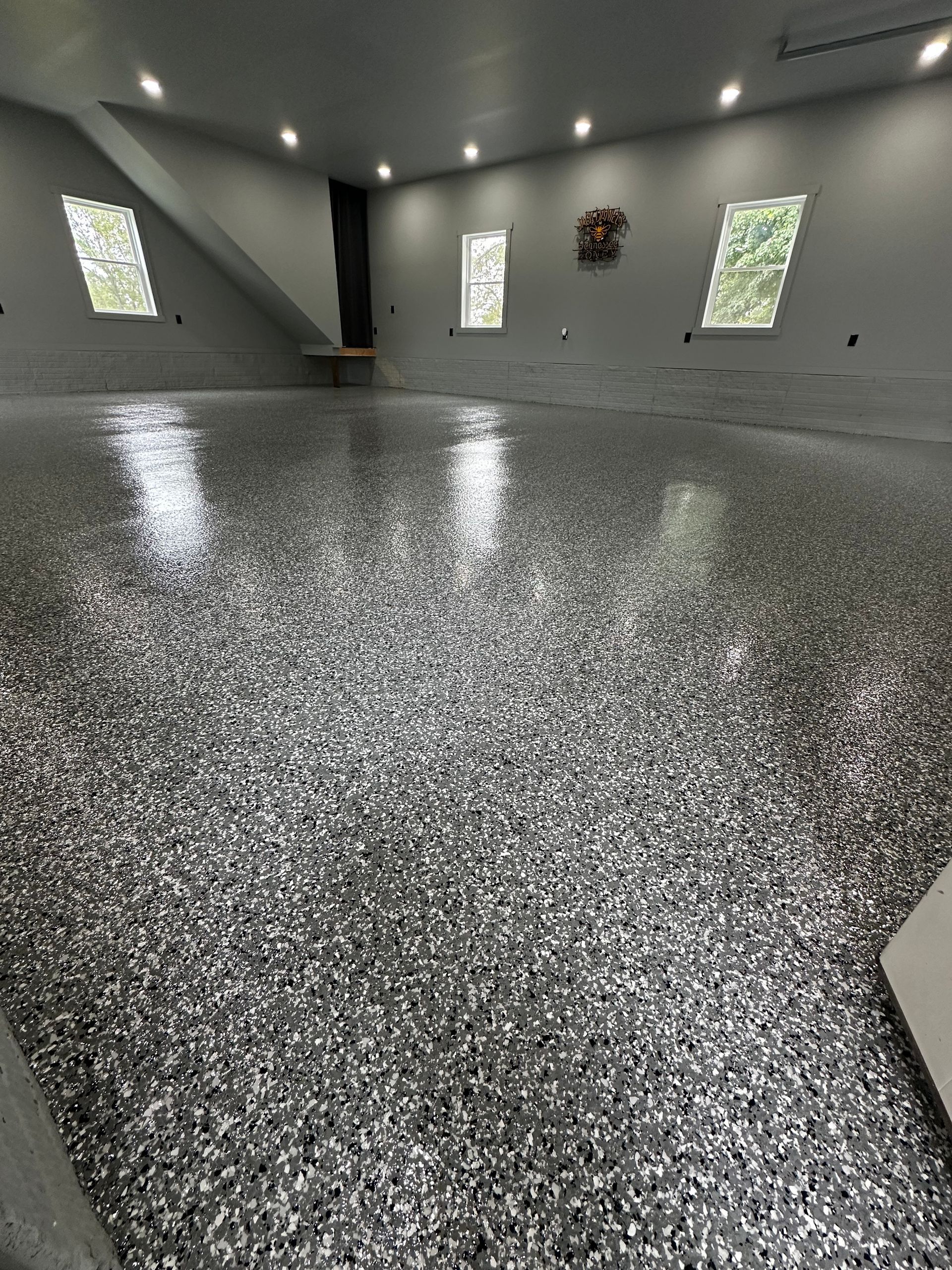Empty gray room with glossy speckled epoxy floor and small windows.