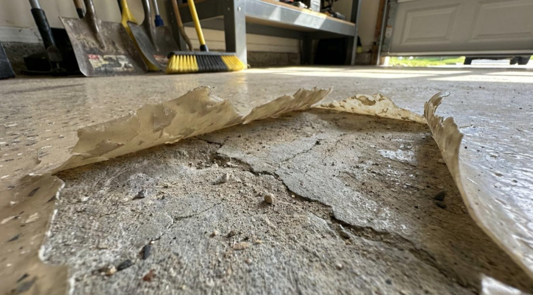 Close-up of a torn concrete slab with crumbling edges on a floor, under a cabinet.