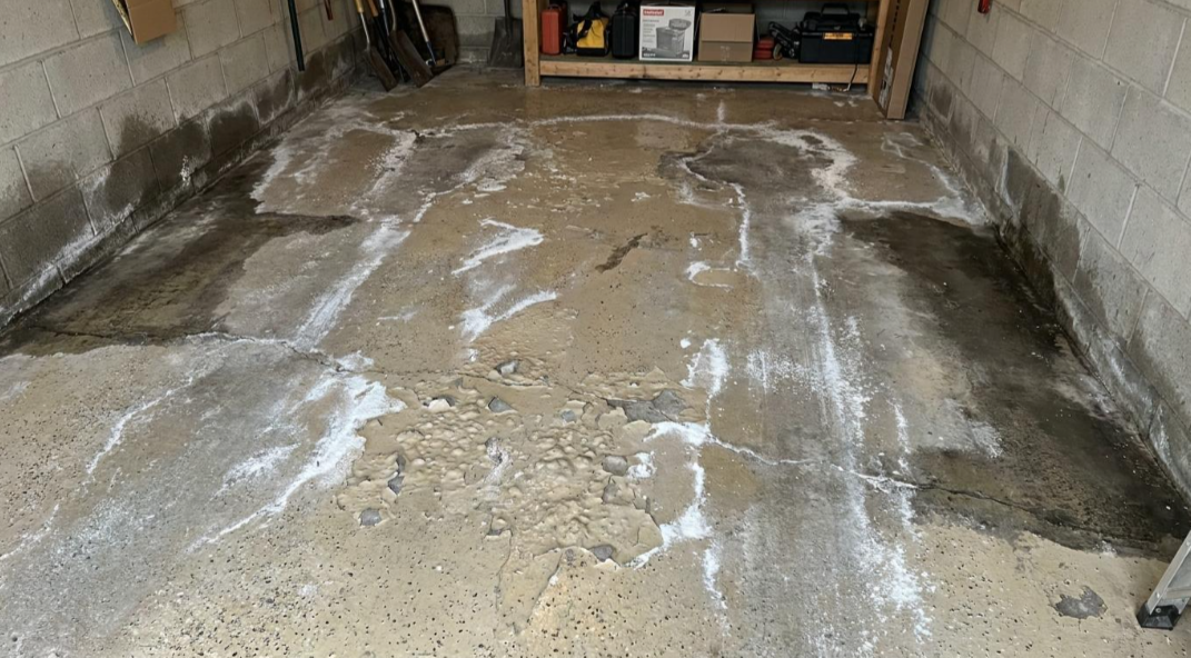Bare concrete floor in a narrow room, with white patchy residue and damp-looking stains along the edges.