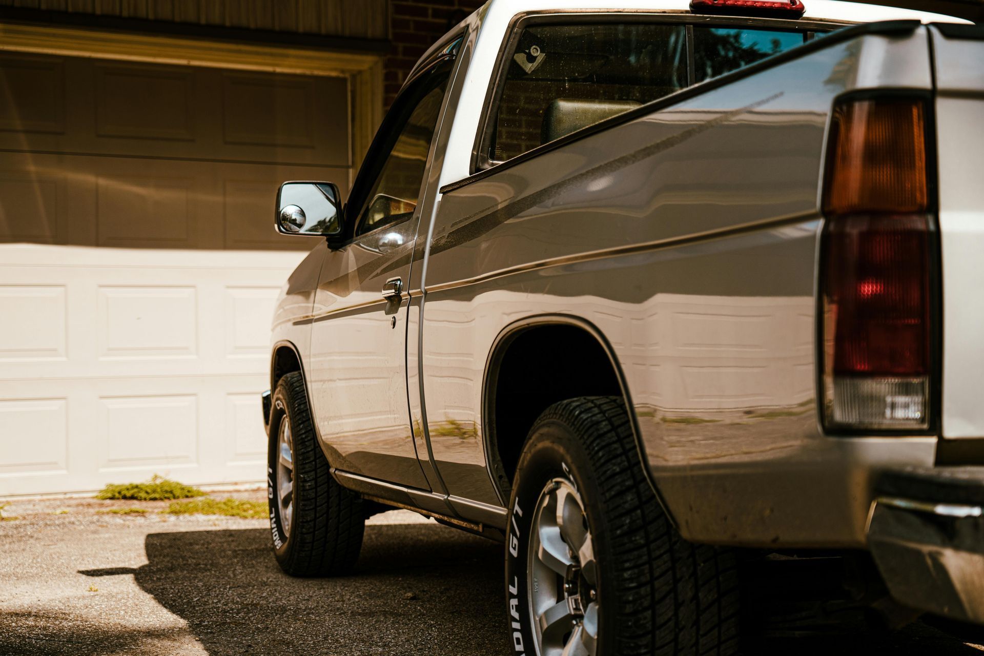 Silver pickup truck parked in a driveway at dusk beside a white garage door