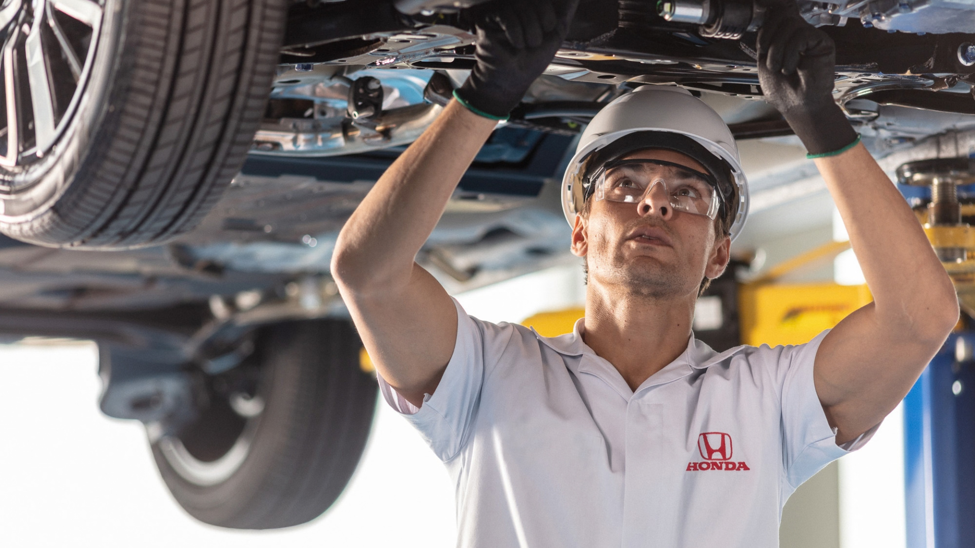 Mechanic in white uniform inspecting vehicle underside in auto repair shop