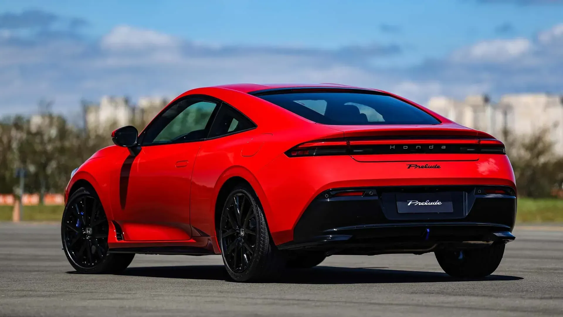 Red sports coupe parked on a road, rear three-quarter view, with black wheels and a bright blue sky.