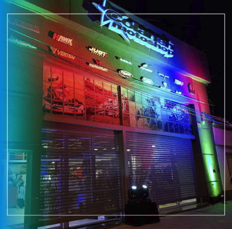 Fachada de tienda colorida iluminada con luces de neón por la noche, con ventanas cerradas y letreros luminosos.