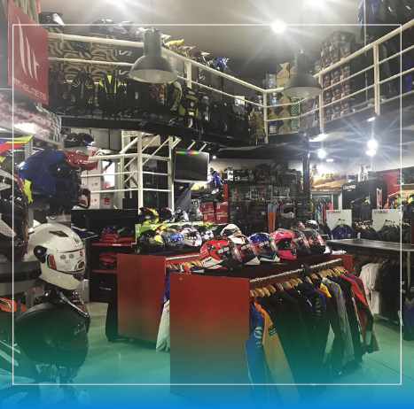 Tienda de equipamiento para motociclistas en interiores con cascos, chaquetas y accesorios en percheros y estantes.