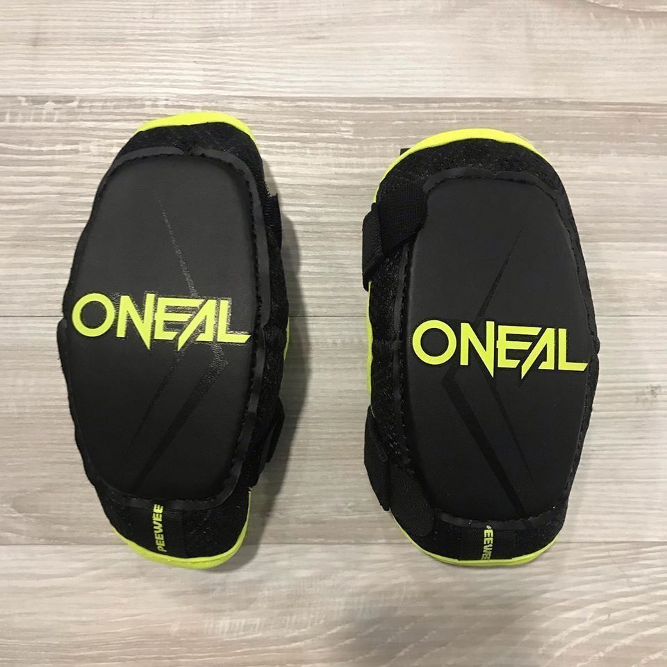 Par de protectores negros O'Neal con ribete amarillo neón sobre una superficie de madera clara.