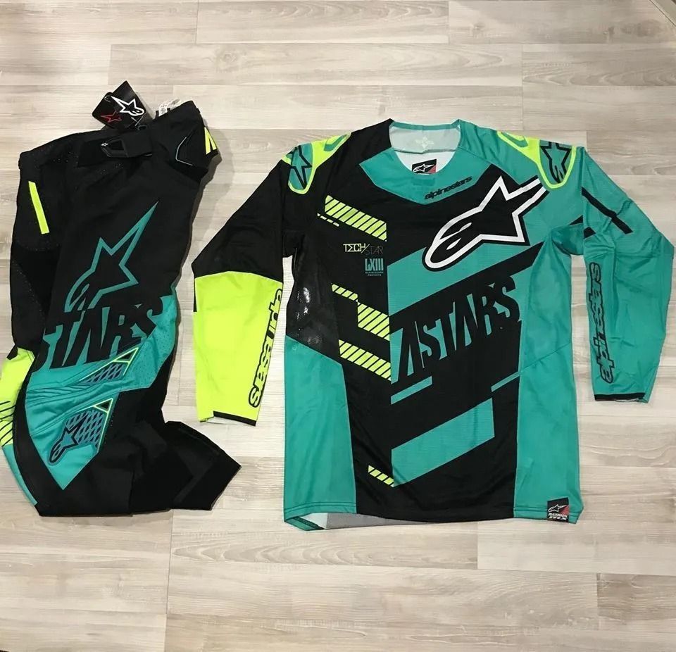 Dos conjuntos de motocross de color verde azulado, negro y neón, extendidos sobre un suelo de madera.