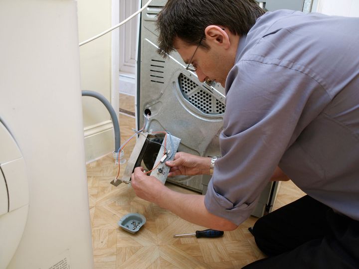 A man is fixing a refrigerator with a screwdriver.