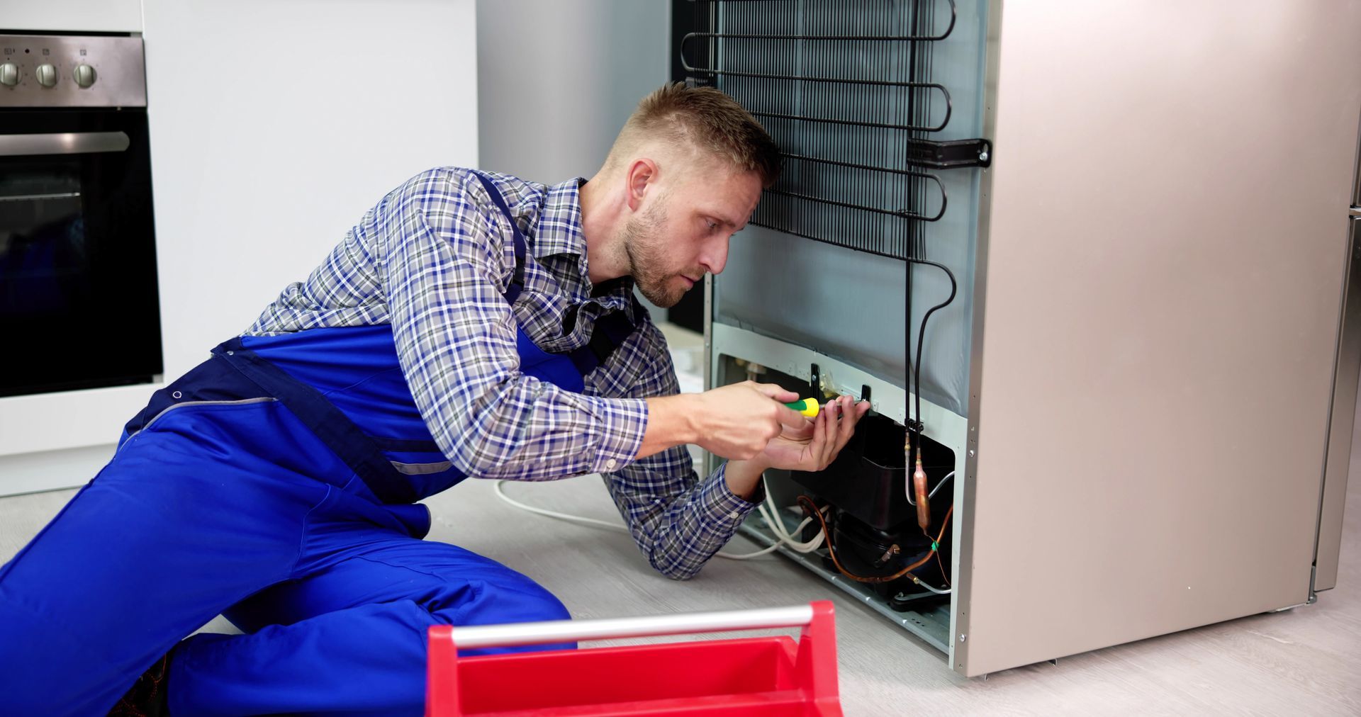 A man is fixing a washing machine with a screwdriver.