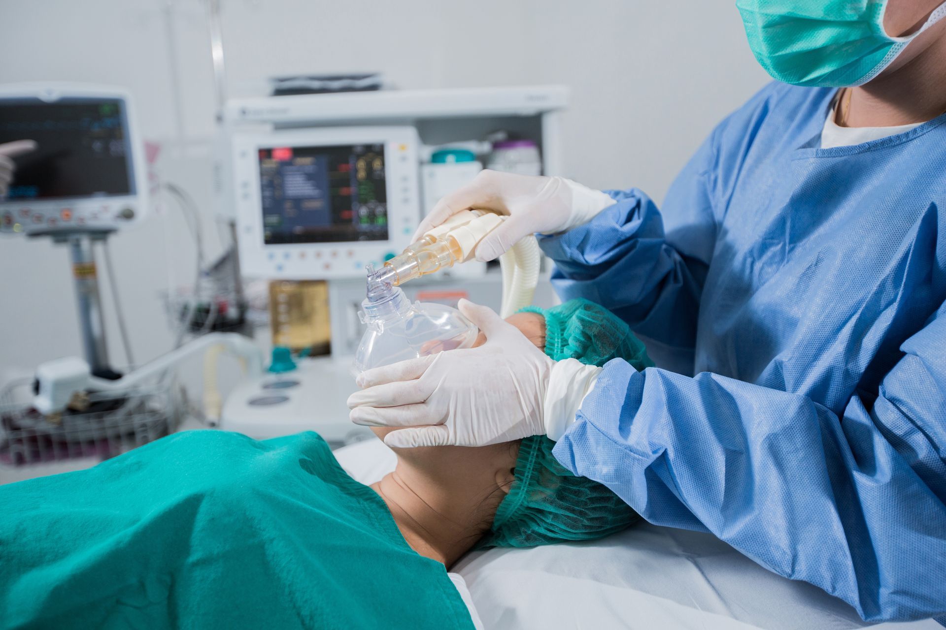 Medical staff in blue scrubs using a bag-mask anesthesia device on a patient in an operating room