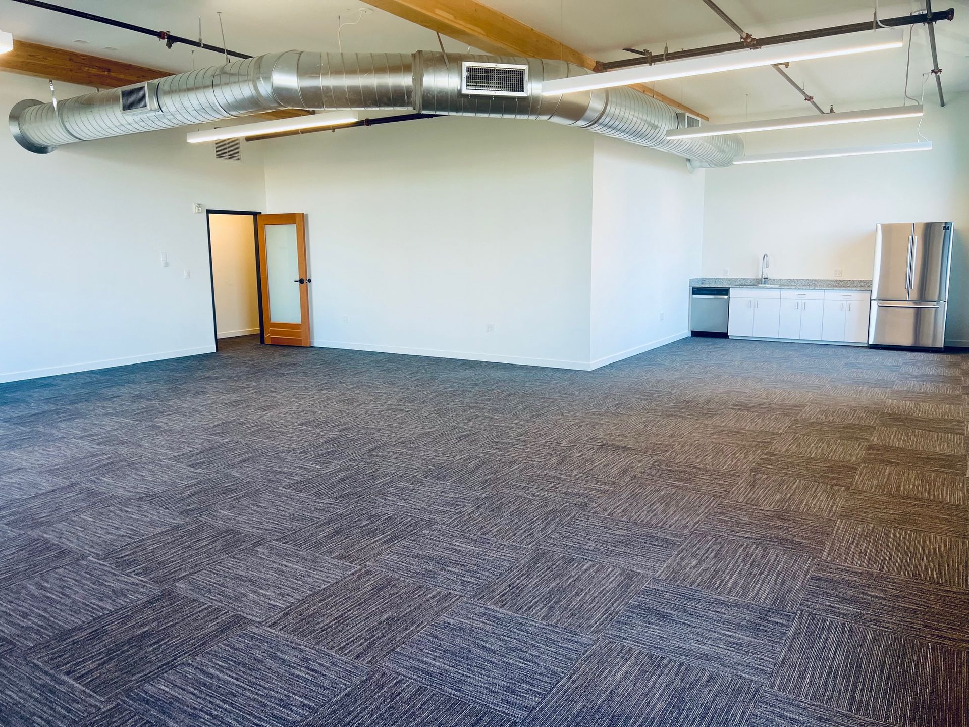 A large empty room with a carpeted floor and a refrigerator.