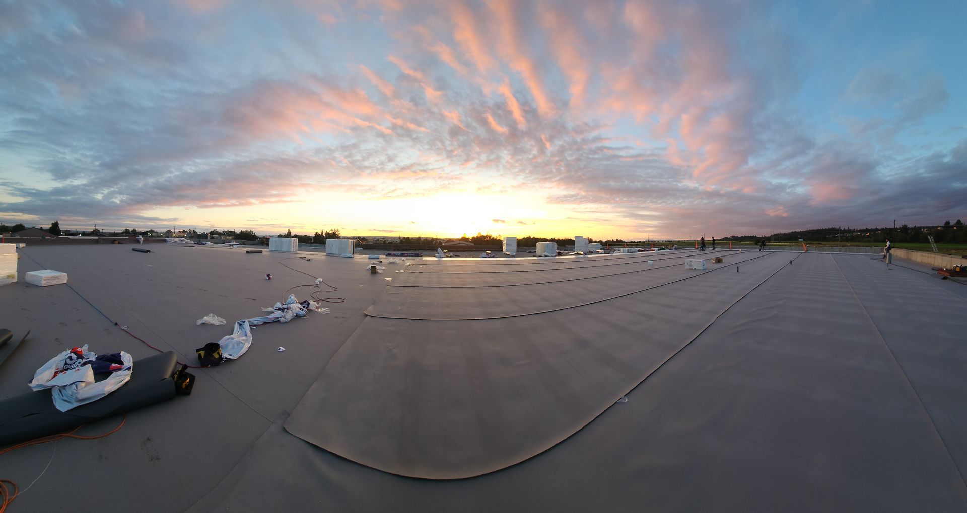Panoramic view of a flat commercial roof surface during a vibrant sunset with clouds, featuring construction materials.