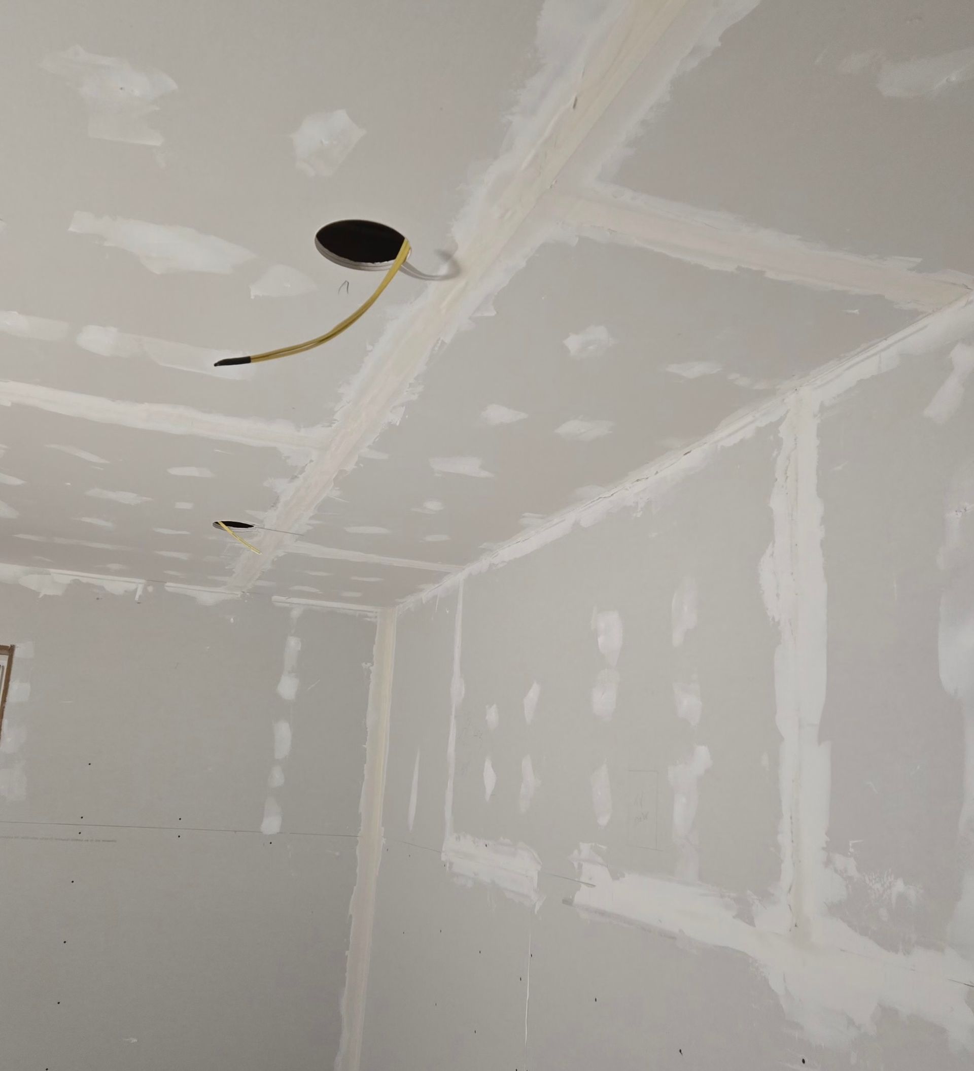 A room interior showing a ceiling and walls with newly installed, taped, and mudded drywall.