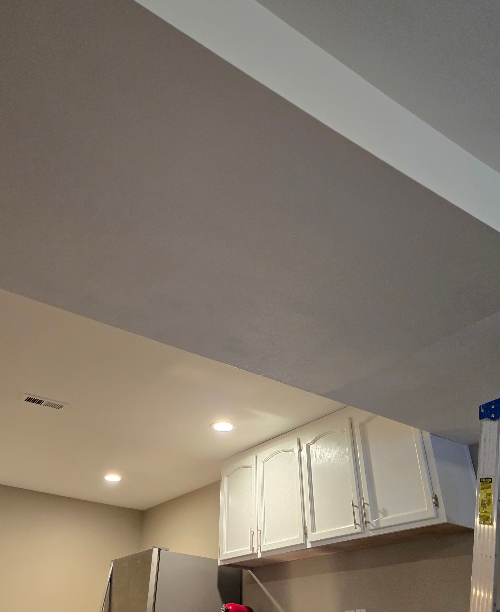 A low-angle view of a kitchen ceiling featuring a soffit, recessed lighting, and white cabinets mounted to the wall.