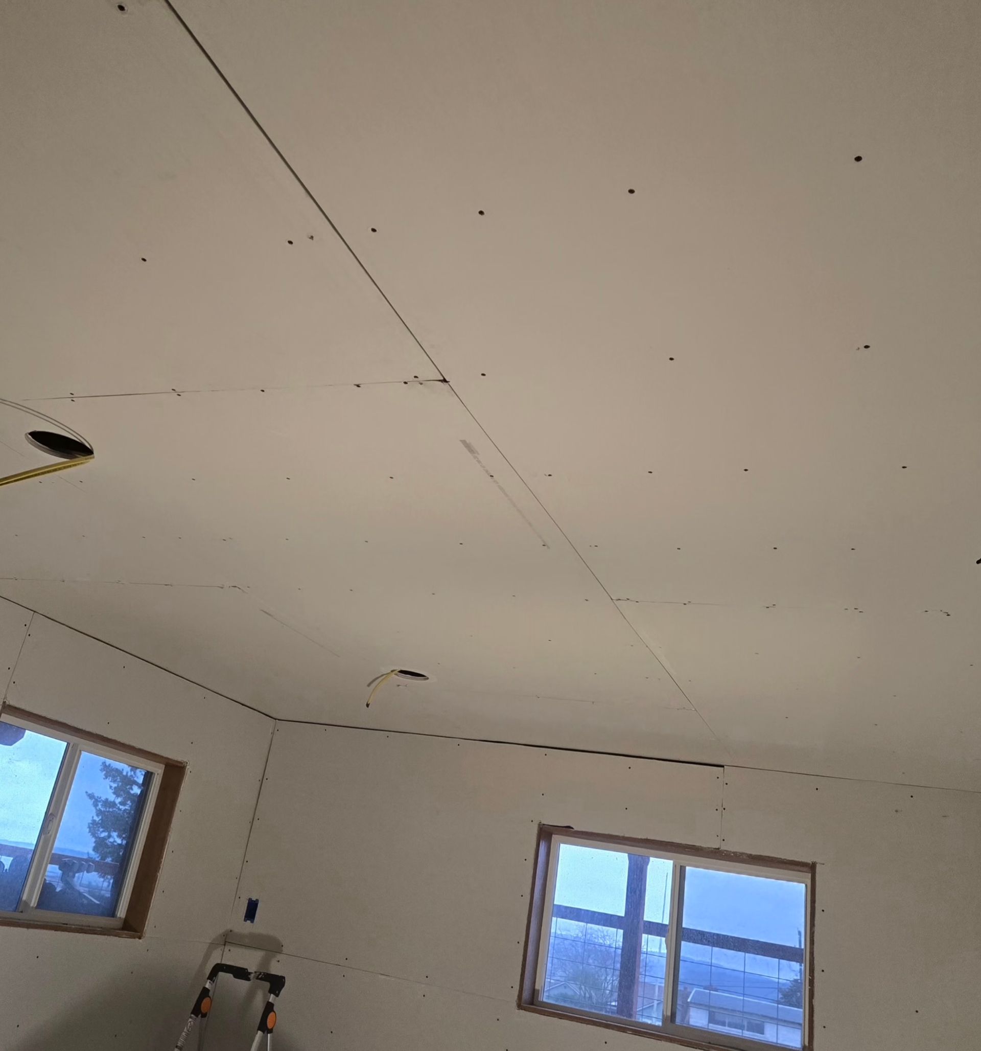 A room under renovation with bare drywall panels attached to the ceiling and walls, showing visible screw patterns.