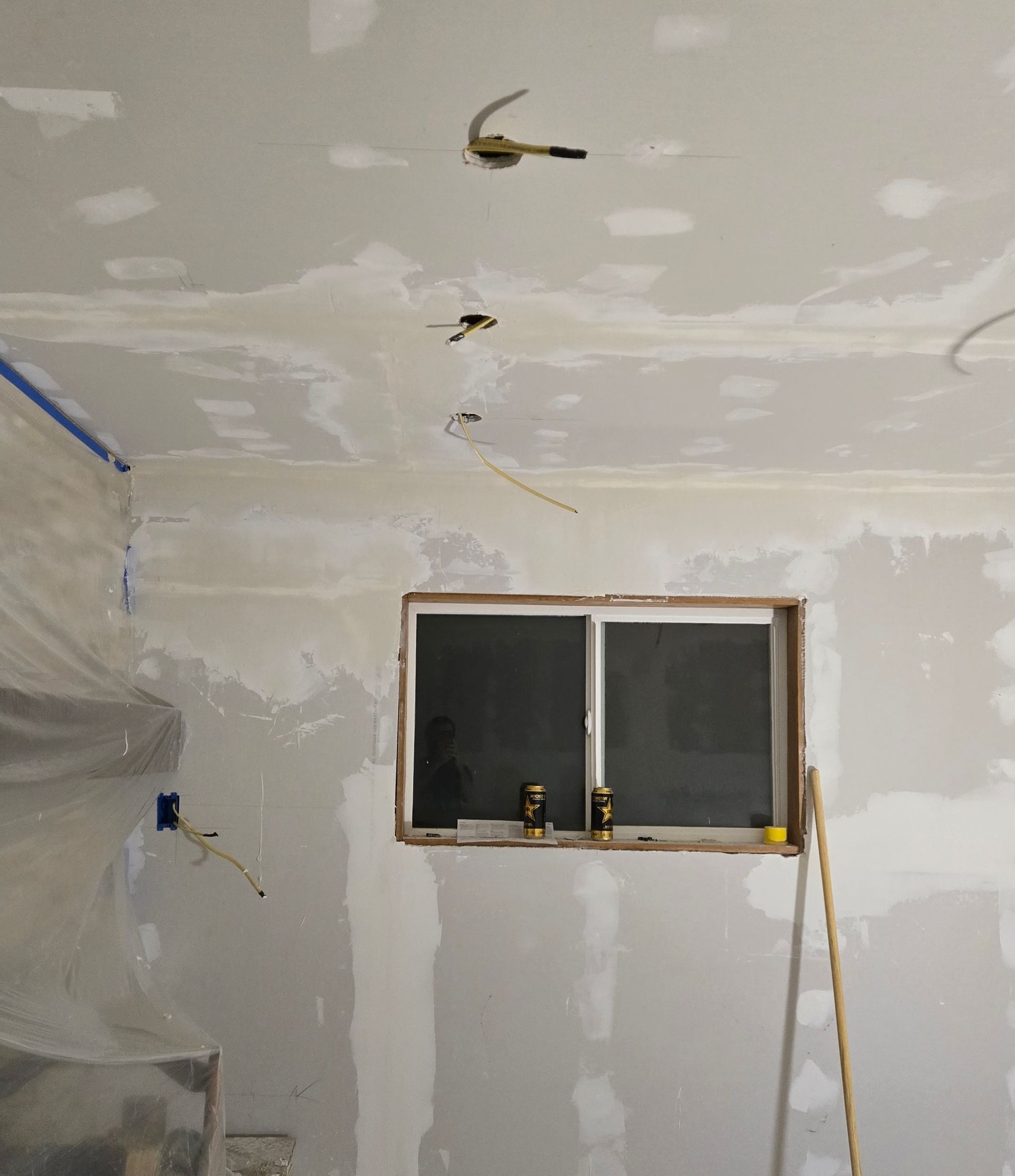 A room under renovation with drywall patches on the walls and ceiling and exposed electrical wiring hanging from holes.